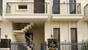 Un immeuble à plusieurs étages, avec un escalier menant à l’entrée, une allée bordée de portails et une enseigne indiquant « Stay & Royal ».