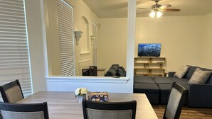 A dining area with a wooden table and chairs, a sofa, and a television in the background. - 3-bedroom house in fabulous Helotes with AC (Helotes)