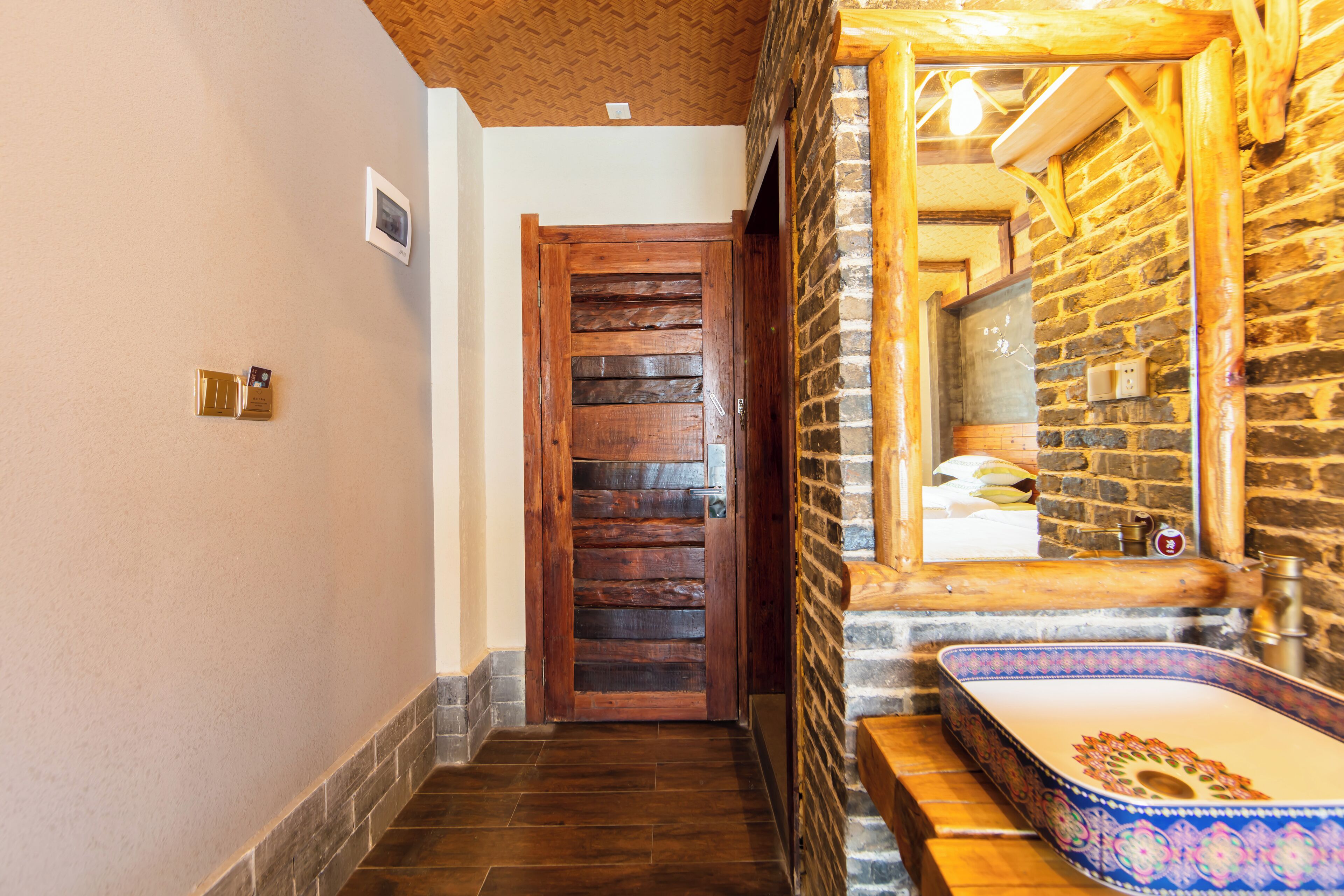 Un estrecho pasillo con una puerta de madera, una pared de piedra y un baño con lavamanos y espejo.