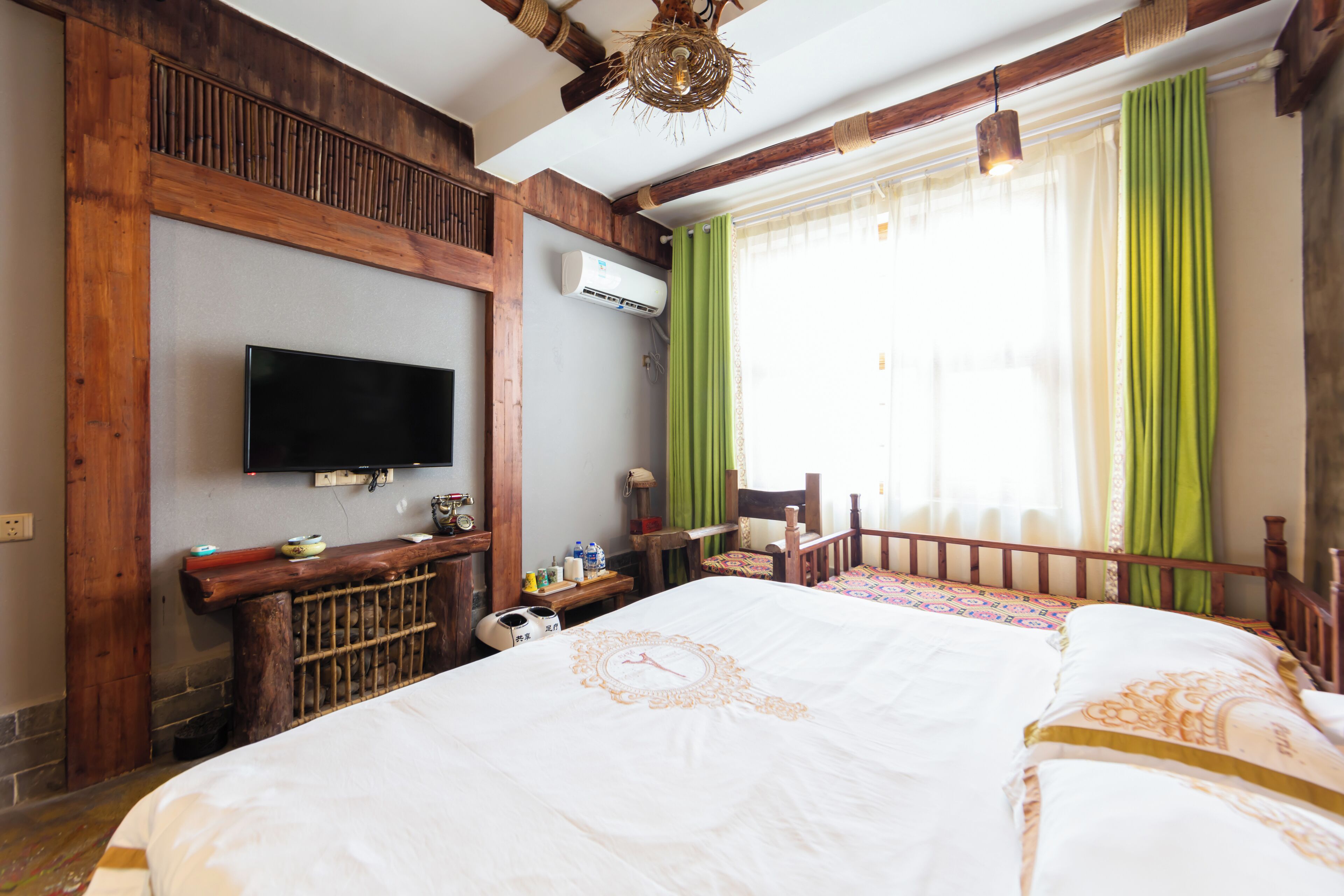 A hotel room with a large bed, a television mounted on the wall, a wooden headboard, and a window with green curtains.