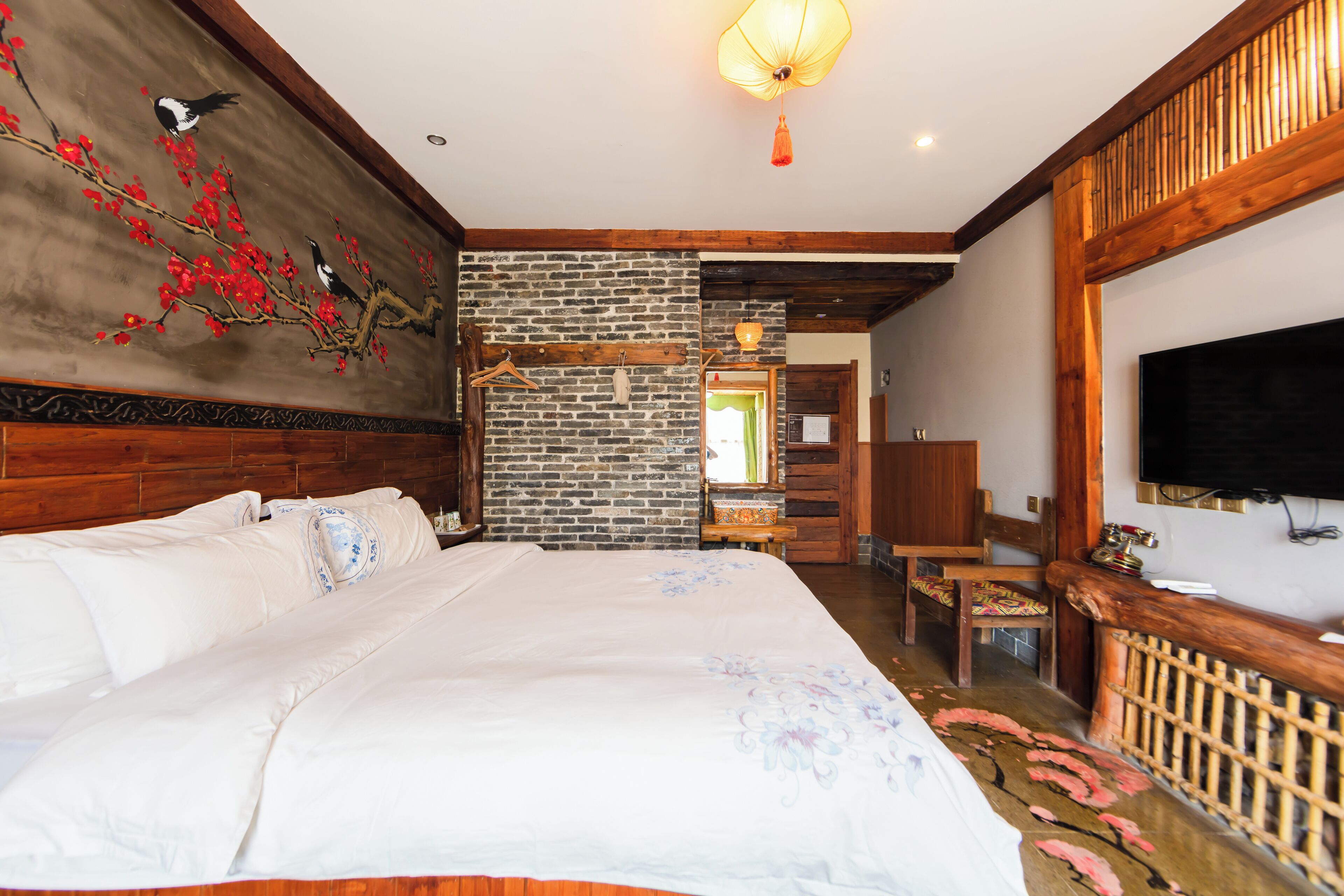 Un dormitorio con una cama grande, cabecera de madera, pared de ladrillo, lámpara colgante y televisor en la pared.