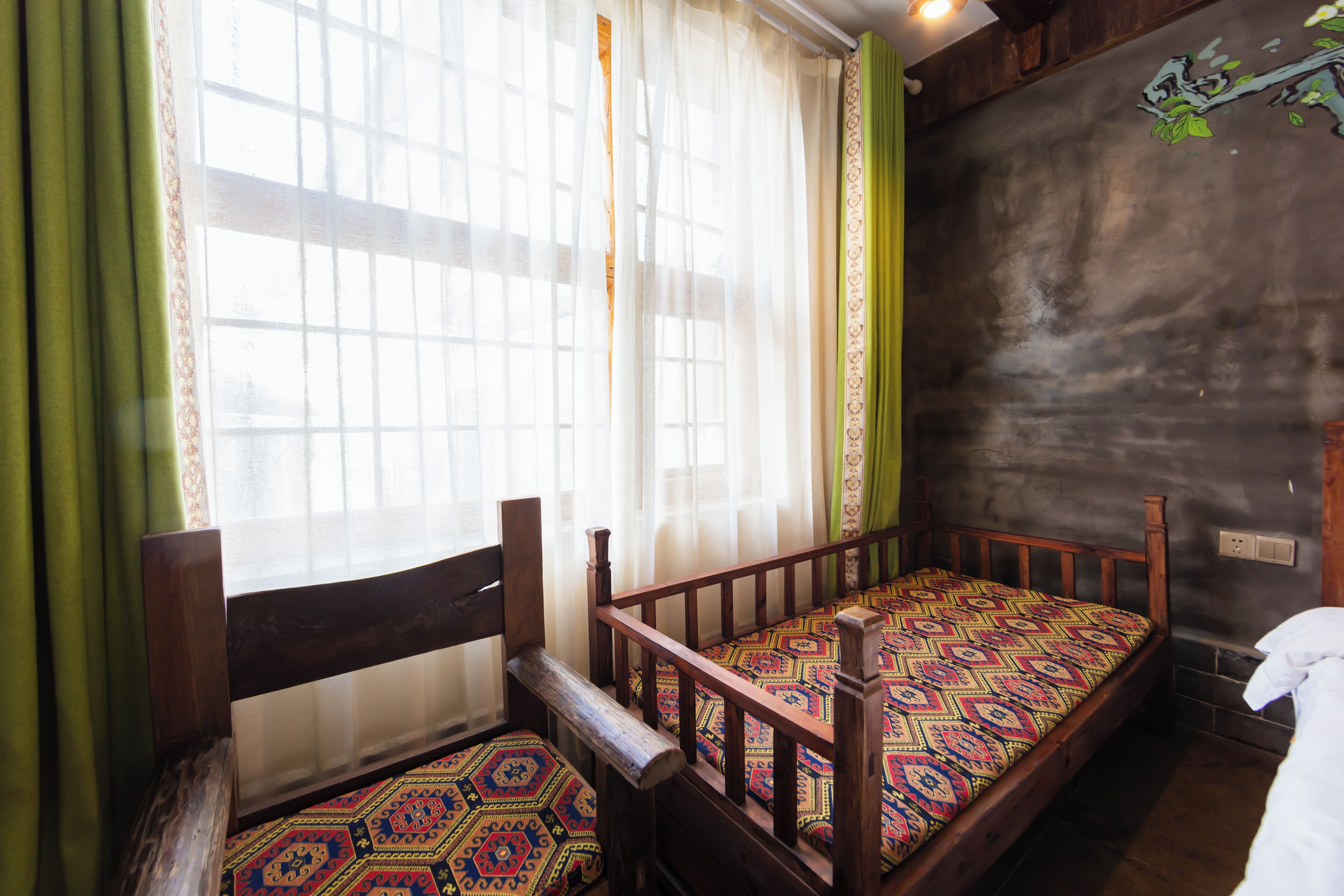 A room with a wooden bed, a window with sheer curtains, and a green curtain.