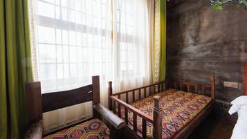 A room with a wooden bed, a window with sheer curtains, and a green curtain.
