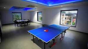 A room with a ping pong table, a dining table with chairs, and large windows with a view of buildings. - Amber Villa By Spandan Holiday Homes (Trimbak)