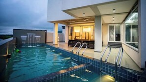 A rooftop swimming pool with a modern design, a lounge area with seating, and a glass-enclosed room. - Amber Villa By Spandan Holiday Homes (Trimbak)