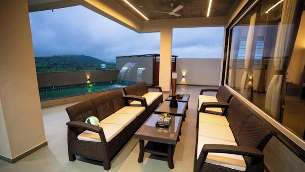 A balcony with wicker furniture, a table, and a view of a waterfall and landscape. - Amber Villa By Spandan Holiday Homes (Trimbak)