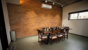 A dining area with a brick wall, a round table, and chairs. - Amber Villa By Spandan Holiday Homes (Trimbak)