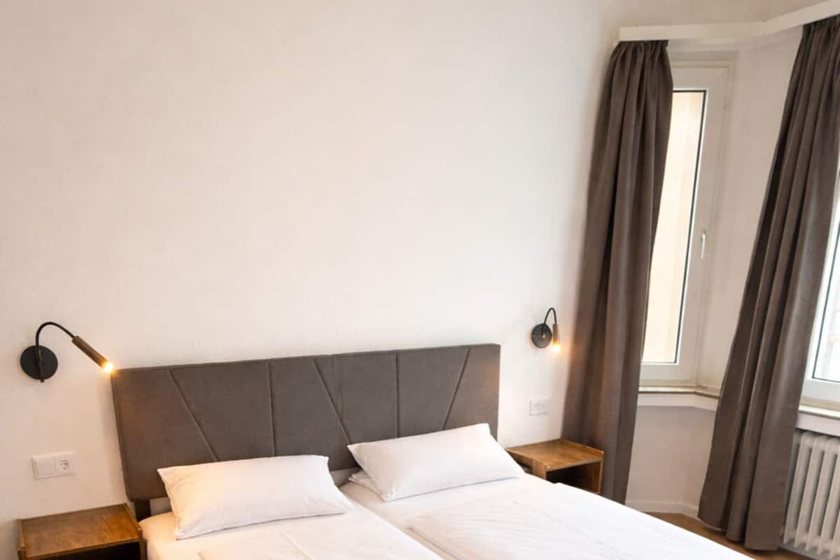 A double bed with a grey headboard, two bedside tables, and a window with curtains.