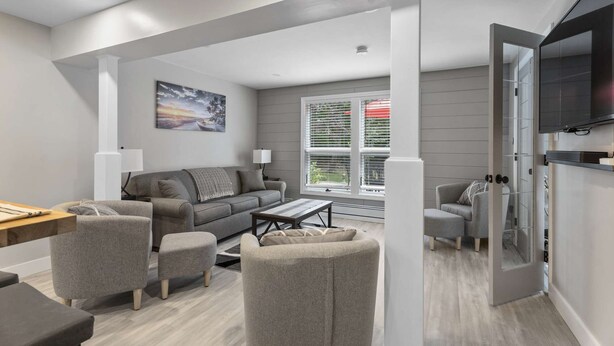 Ein modernes Wohnzimmer mit einem grauen Sofa, zwei Sesseln, einem Couchtisch und einem an der Wand befestigten Fernseher.