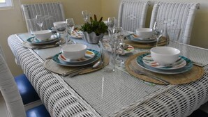 A dining table set with white plates, bowls, cutlery, and glasses, surrounded by wicker chairs. - Punta Cana Beach Luxury apartment 2 bedroom 4 minute walk to beach (Punta Cana)