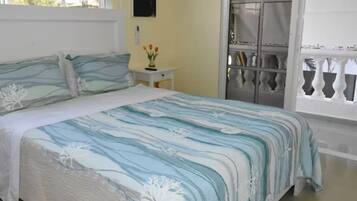 Un dormitorio con cama, mesita de noche, ventana con vista a un balcón y un reloj en la pared.