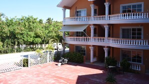 A multi-story building with a balcony, columns, and a fenced patio area. - Punta Cana Beach Luxury apartment 2 bedroom 4 minute walk to beach (Punta Cana)
