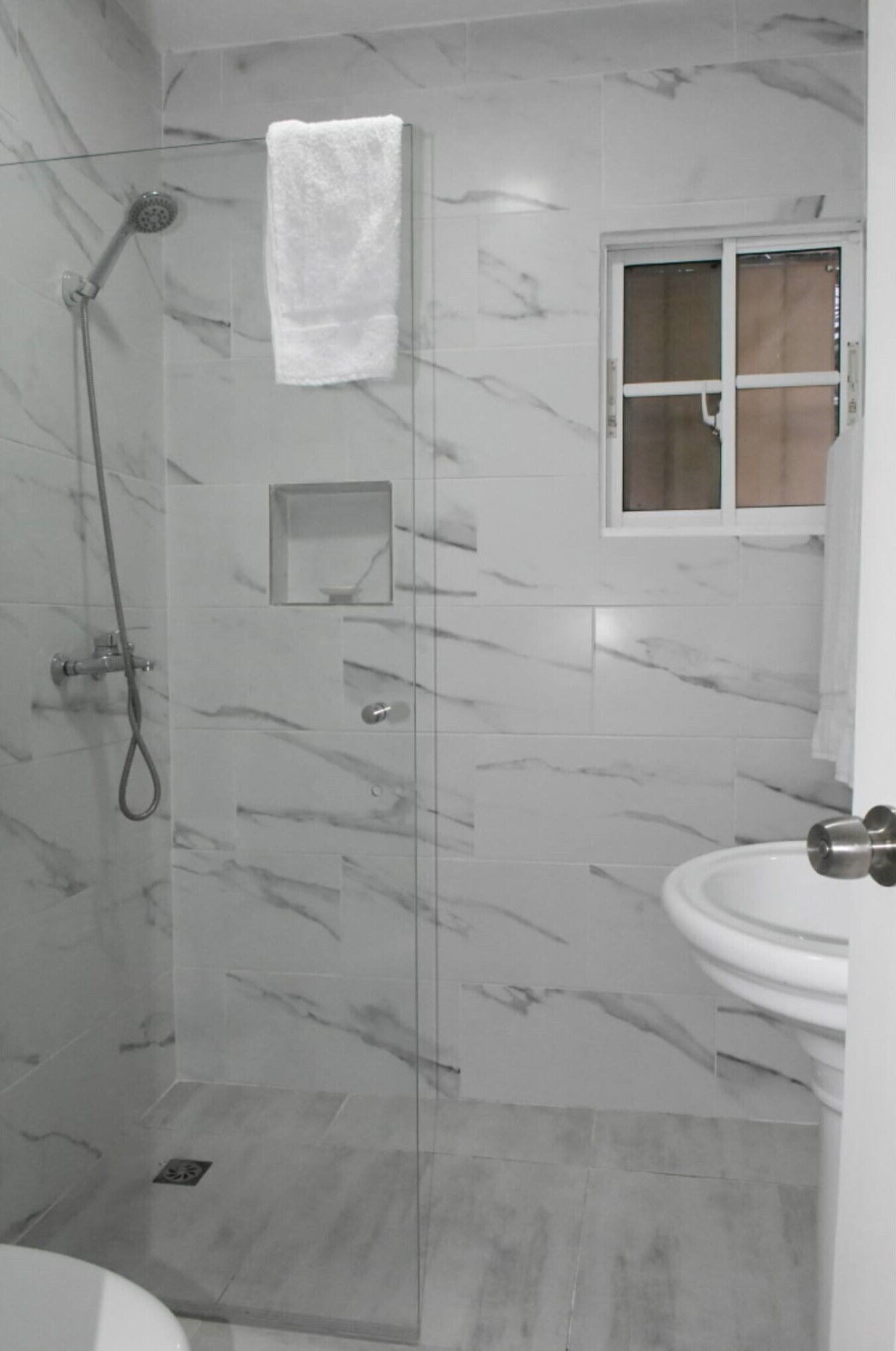 Ein Badezimmer mit einer Duschkabine, einem weißen Waschbecken und einem kleinen Fenster.