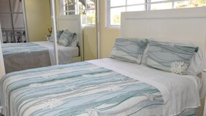 A bedroom with a bed featuring a striped bedspread and matching pillows, a white headboard, and a window with a view of the outdoors. - Punta Cana Beach Luxury apartment 2 bedroom 4 minute walk to beach (Punta Cana)