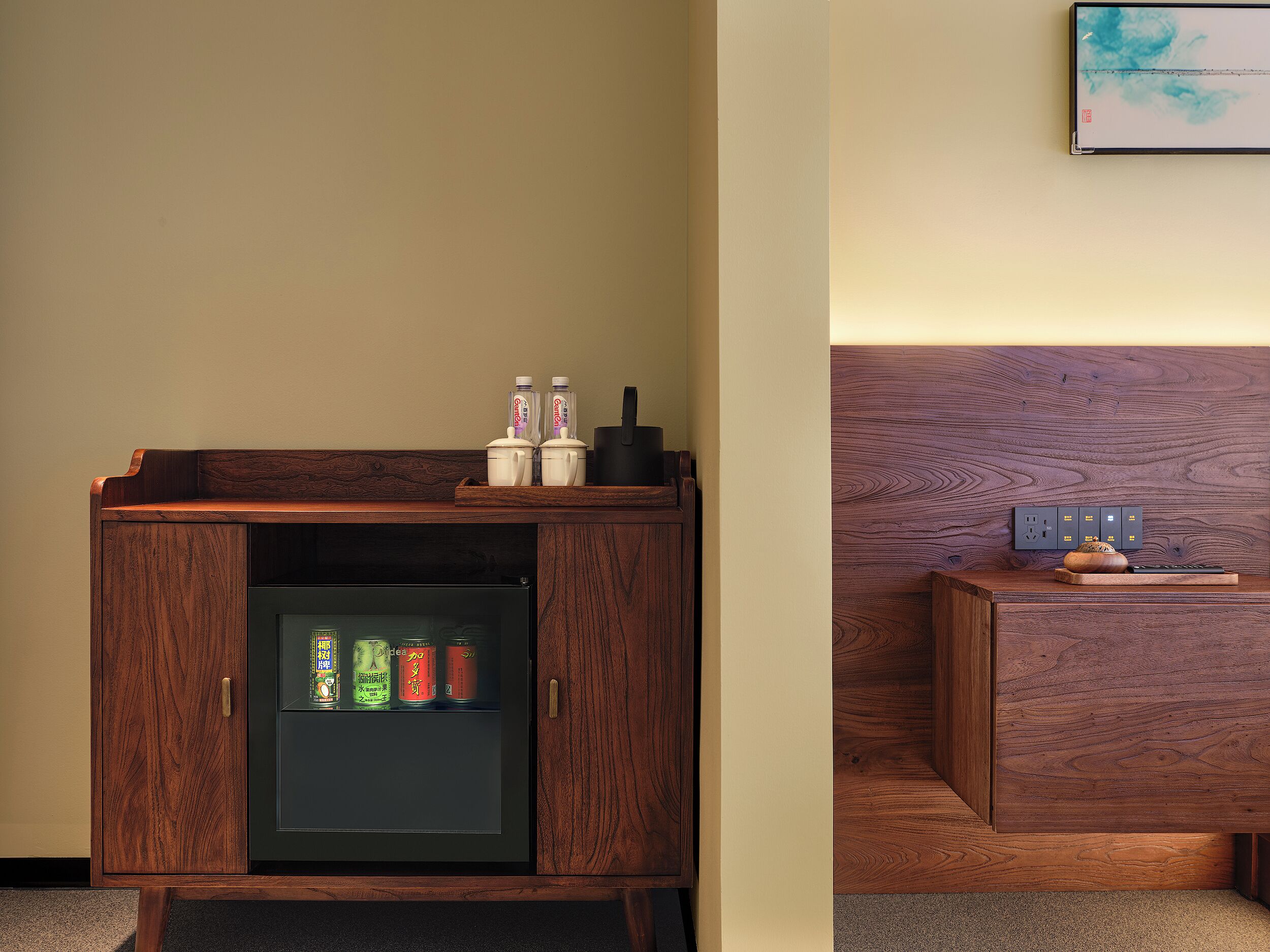 Een houten kast met een geïntegreerde minibar, een stekkerdoos en een klein tafeltje met een decoratief object.