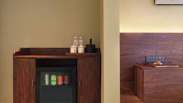 Een houten kast met een geïntegreerde minibar, een stekkerdoos en een klein tafeltje met een decoratief object.