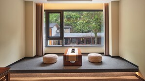 Ein Zimmer mit großem Fenster, einem Holztisch, zwei Korbsesseln und einem Teppichboden.