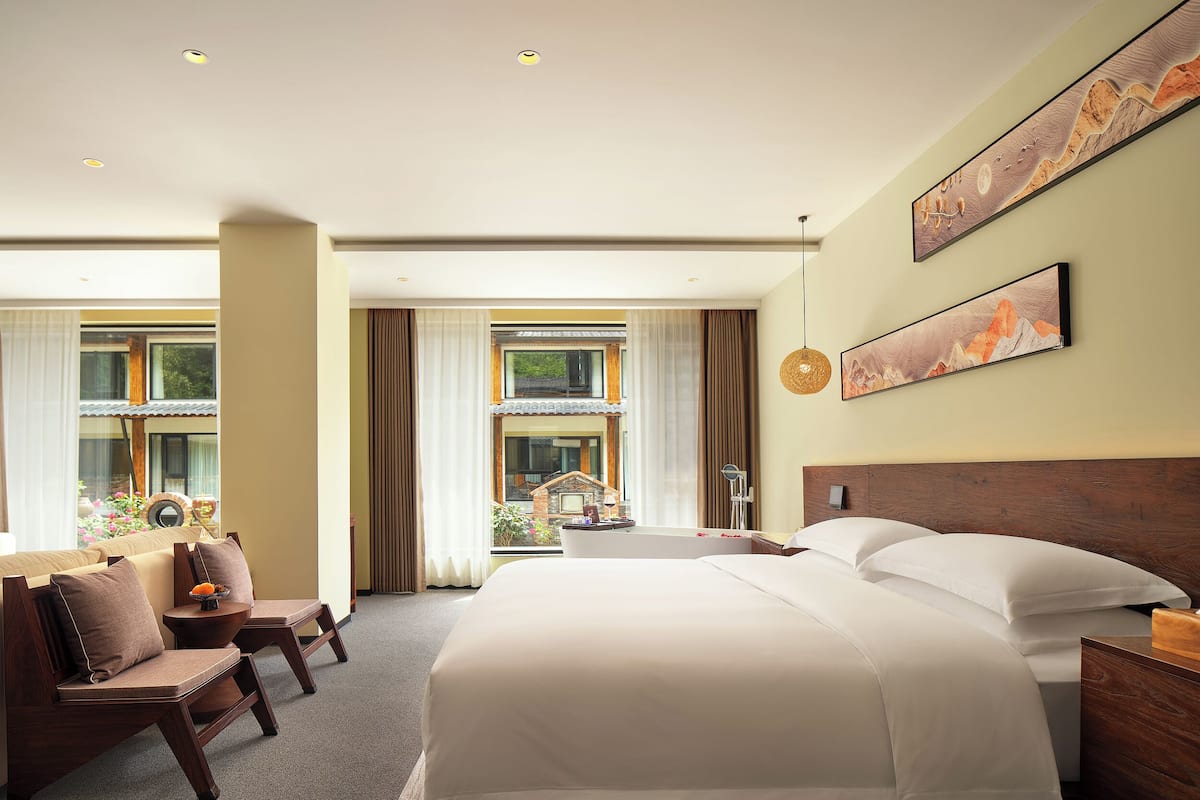 Camera d'albergo con un letto grande, una sedia, una scrivania e vista su una casa tradizionale dalla finestra.