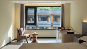 Ein modernes Hotelzimmer mit großem Fenster, einem Bett, einem Schreibtisch und Blick auf traditionelle Architektur.