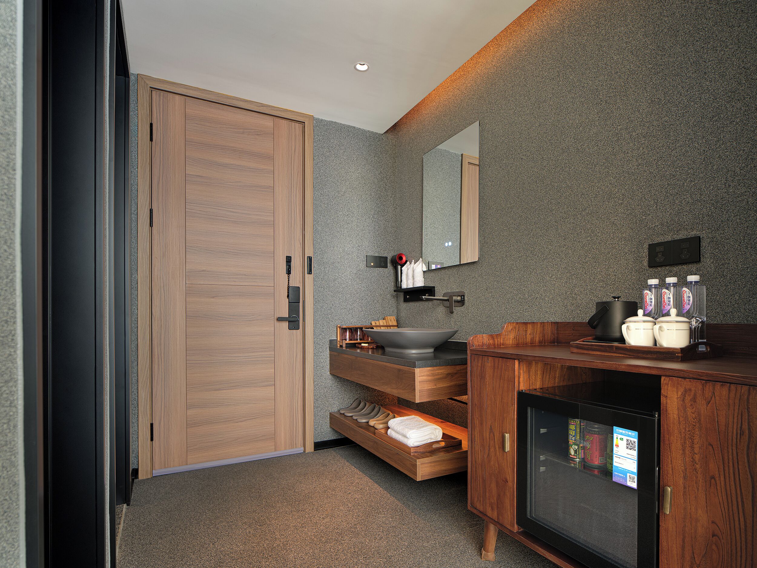A modern bathroom with a wooden door, a sink with a black basin, a mirror, and a cabinet with toiletries.
