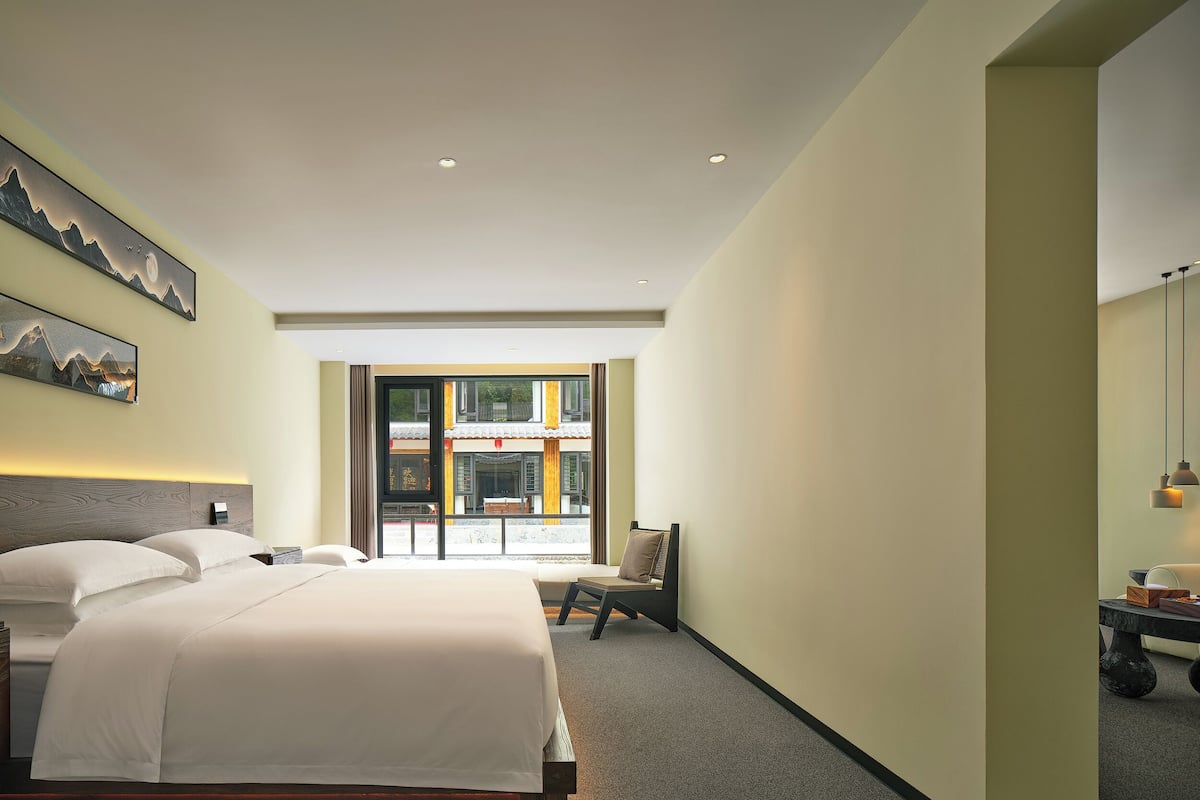Camera d'albergo con un ampio letto, una scrivania e vista su un edificio tradizionale attraverso una porta in vetro.