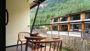 Ein Balkon mit einem Holztisch und Stühlen, der auf einen Fluss und ein Gebäude mit großen Fenstern blickt.