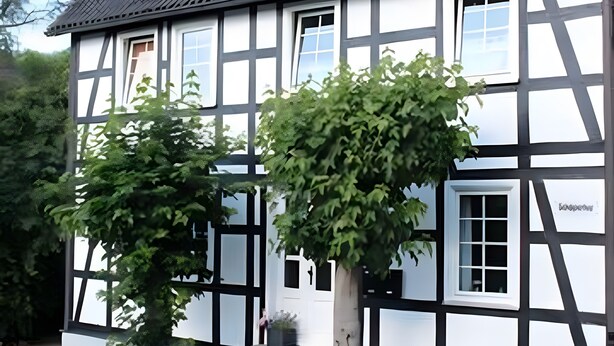 Een klassiek vakwerkhuis met een symmetrische gevel, grote ramen en een verzorgde tuin.