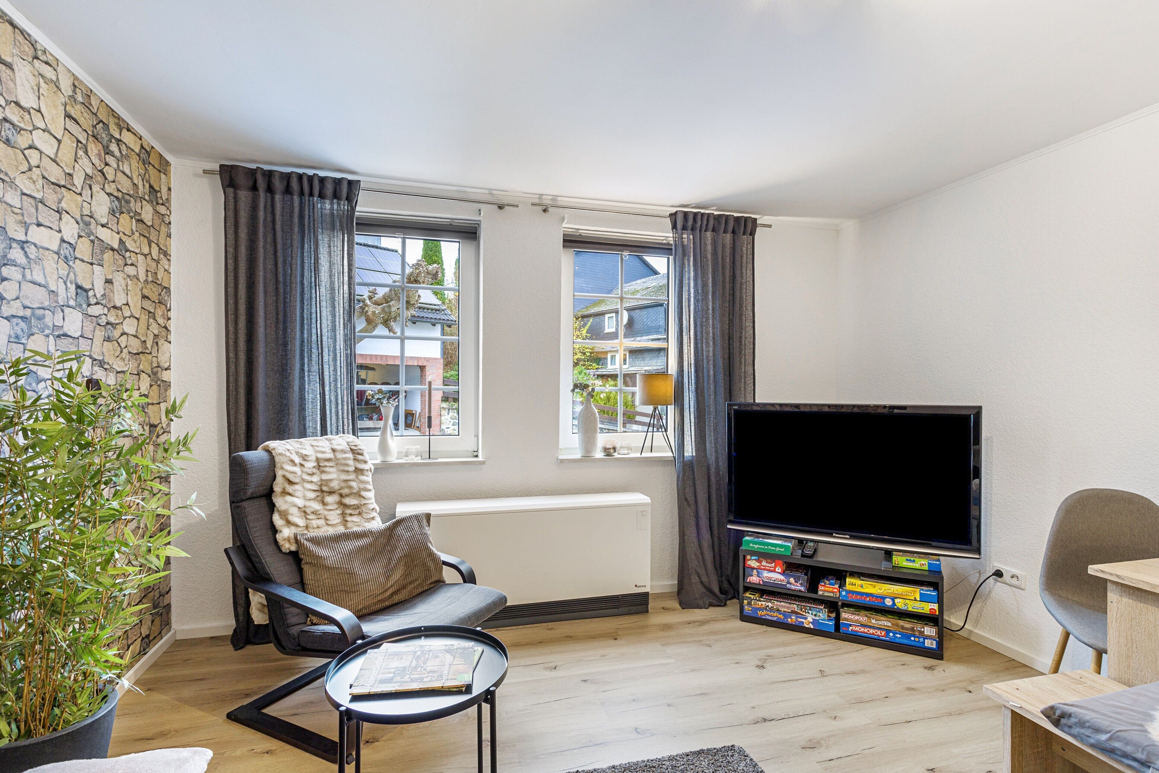 A living room with a stone wall, a large window, a black sofa, a television, and a plant.