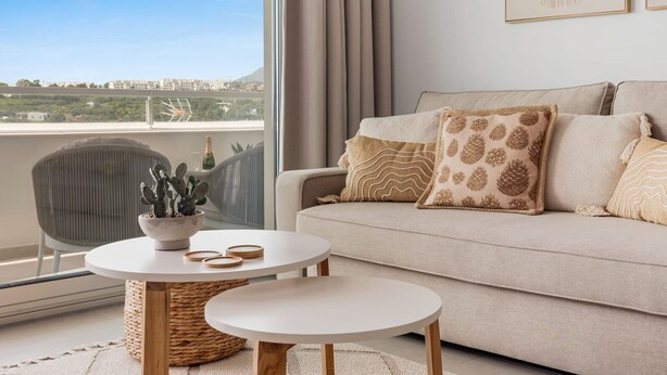 A modern living room with a sofa, two side tables, a potted plant, and a view of the city. - Casa Oceana | Pool - views - gym (Estepona)