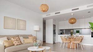A modern living room with a sofa, coffee table, and dining area with wicker chairs. - Casa Oceana | Pool - views - gym (Estepona)