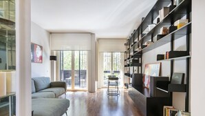 Een moderne woonkamer met een bank, een boekenkast en een eethoek met een tafel en stoelen.