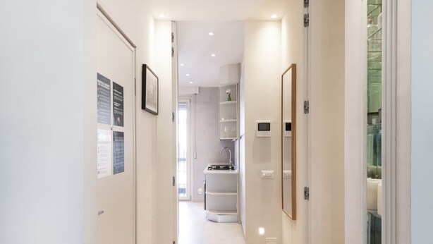 Een smalle gang met een houten vloer die leidt naar een badkamer met een wastafel en planken.