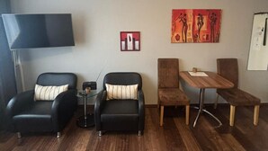 Ein Wohnzimmer mit Flachbildfernseher, zwei schwarzen Ledersesseln, einem kleinen runden Tisch, einem Holz-Couchtisch und einem Gemälde an der Wand.