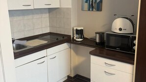 Eine kompakte Küche mit weißen Schränken, einer dunklen Arbeitsplatte, einer Kaffeemaschine und einer Mikrowelle.