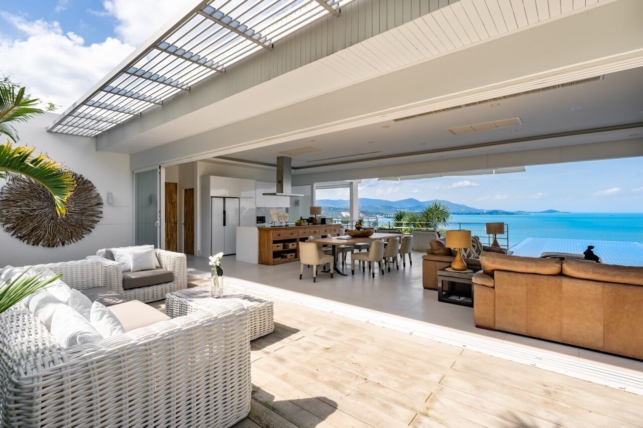 A spacious living area with a large dining table, comfortable seating, and a view of the ocean.