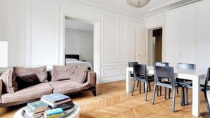 Uma sala de estar moderna com um sofá, uma mesa de jantar com cadeiras e um lustre.