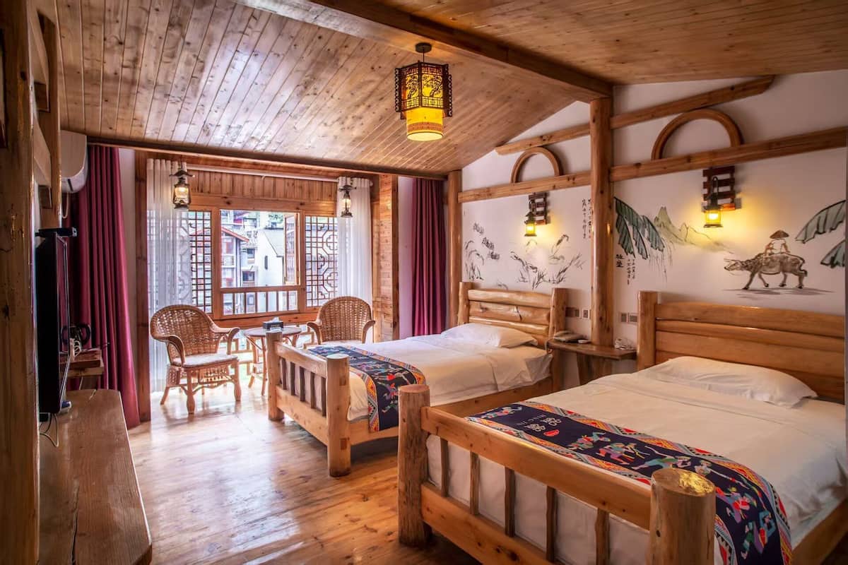 Ein Zimmer mit Holzboden, zwei Betten, einem Esstisch, Stühlen und einem Fenster mit Vorhängen.