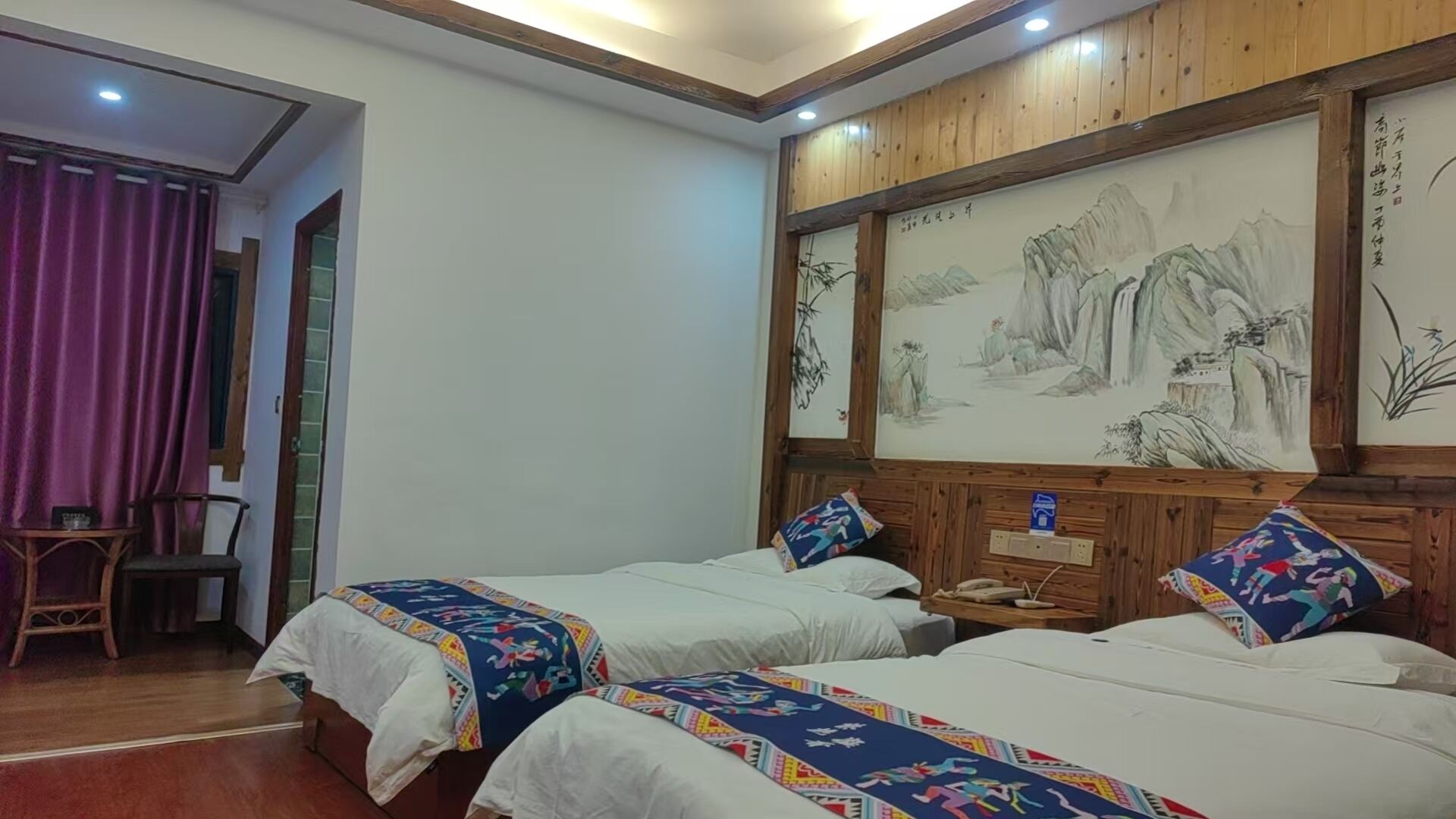 Ein Hotelzimmer mit zwei Betten, einem hölzernen Kopfende mit Kunstwerk, einem kleinen Tisch mit Telefon und einem Stuhl.