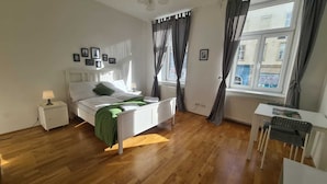 Ein Schlafzimmer mit Bett, Nachttisch, Lampe und Blick auf die Straße durch ein Fenster.
