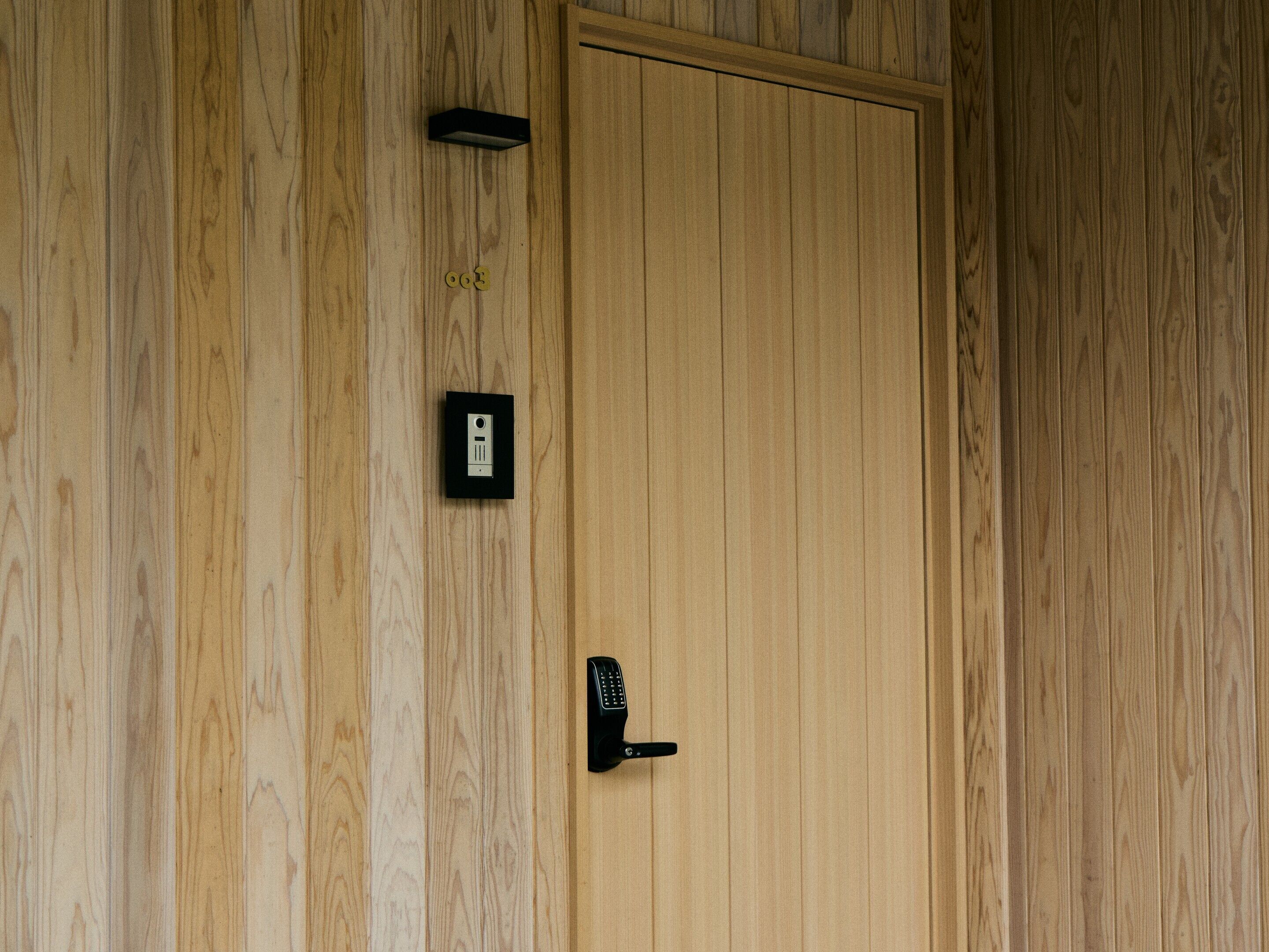 A wooden door with a modern electronic lock and a small, rectangular device mounted on the wall above it.