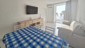 Un dormitorio con cama, escritorio, silla, televisor y balcón con vistas a la playa.