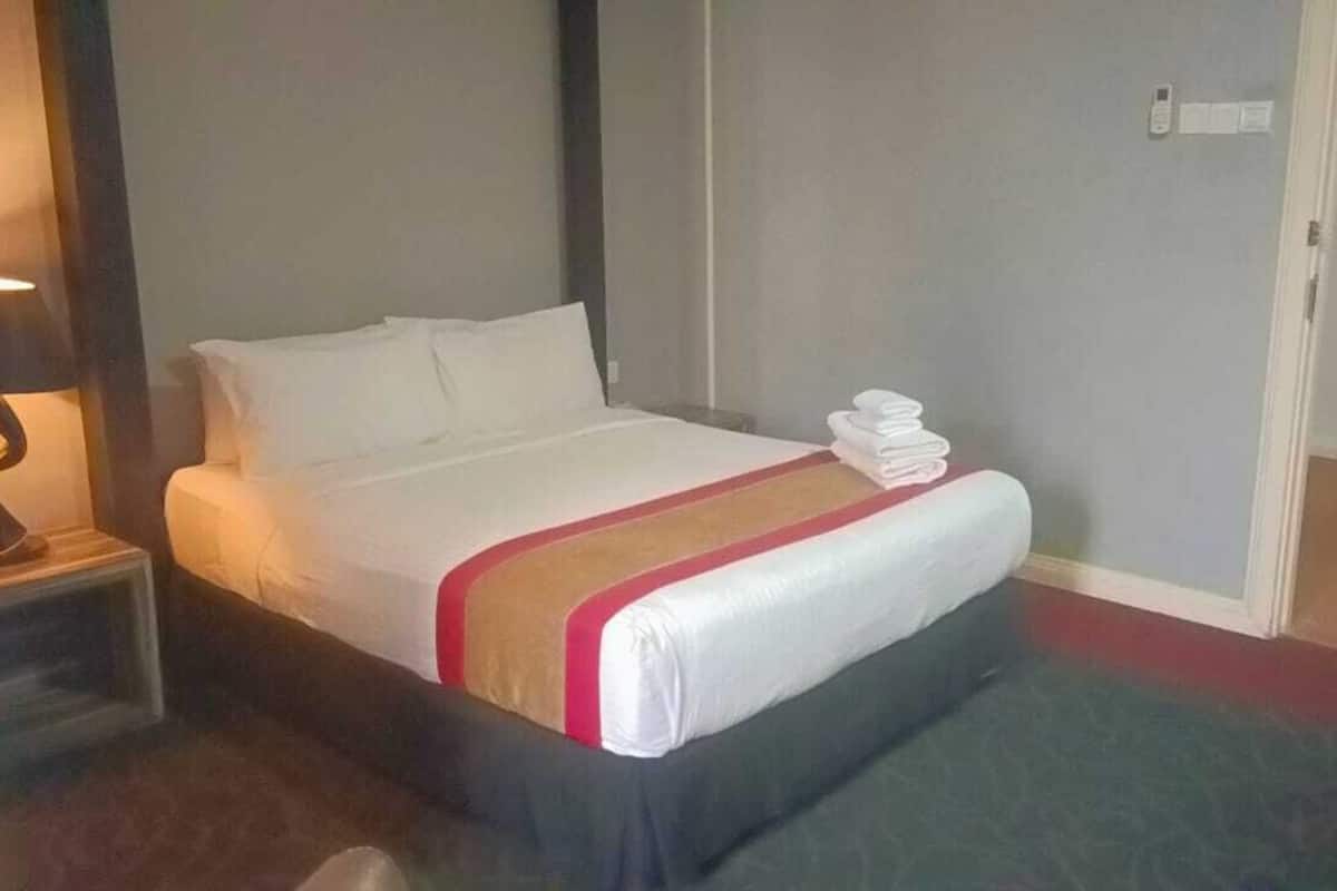 A hotel room with a bed, a nightstand, a lamp, and a folded towel on the bed.