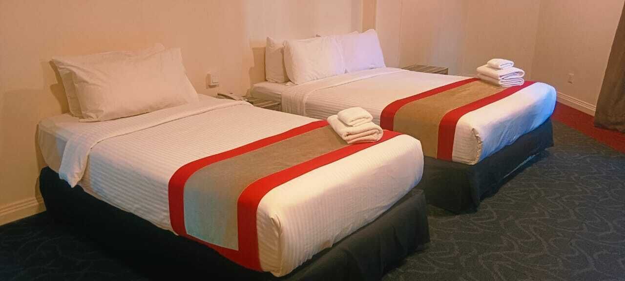 Two twin beds with red and white bedding, a dark carpet, and a white wall.