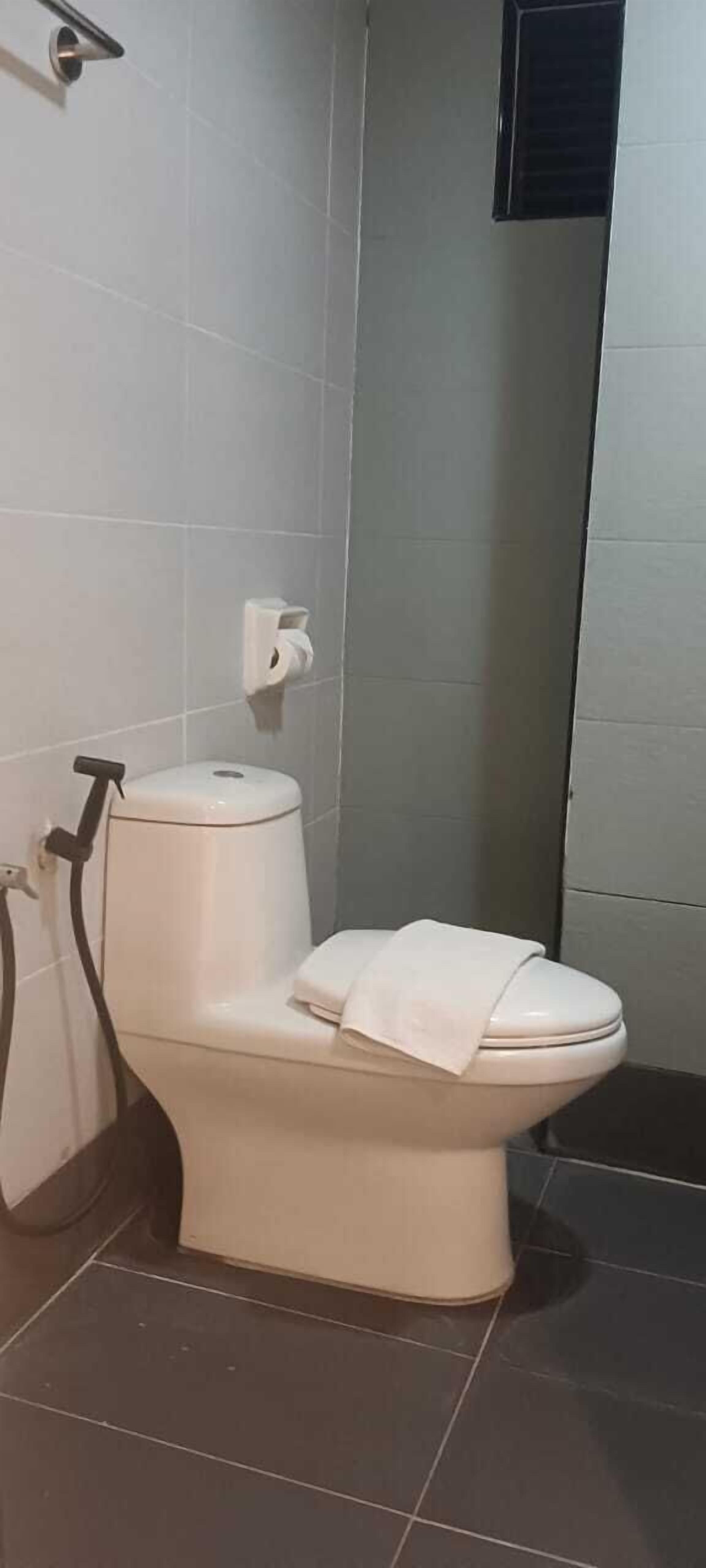 A bathroom with a white toilet, a paper towel dispenser, and a showerhead.