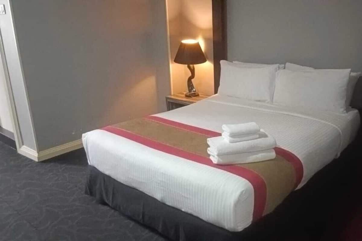 A hotel room with a neatly made bed, a bedside lamp, and a door to the right.