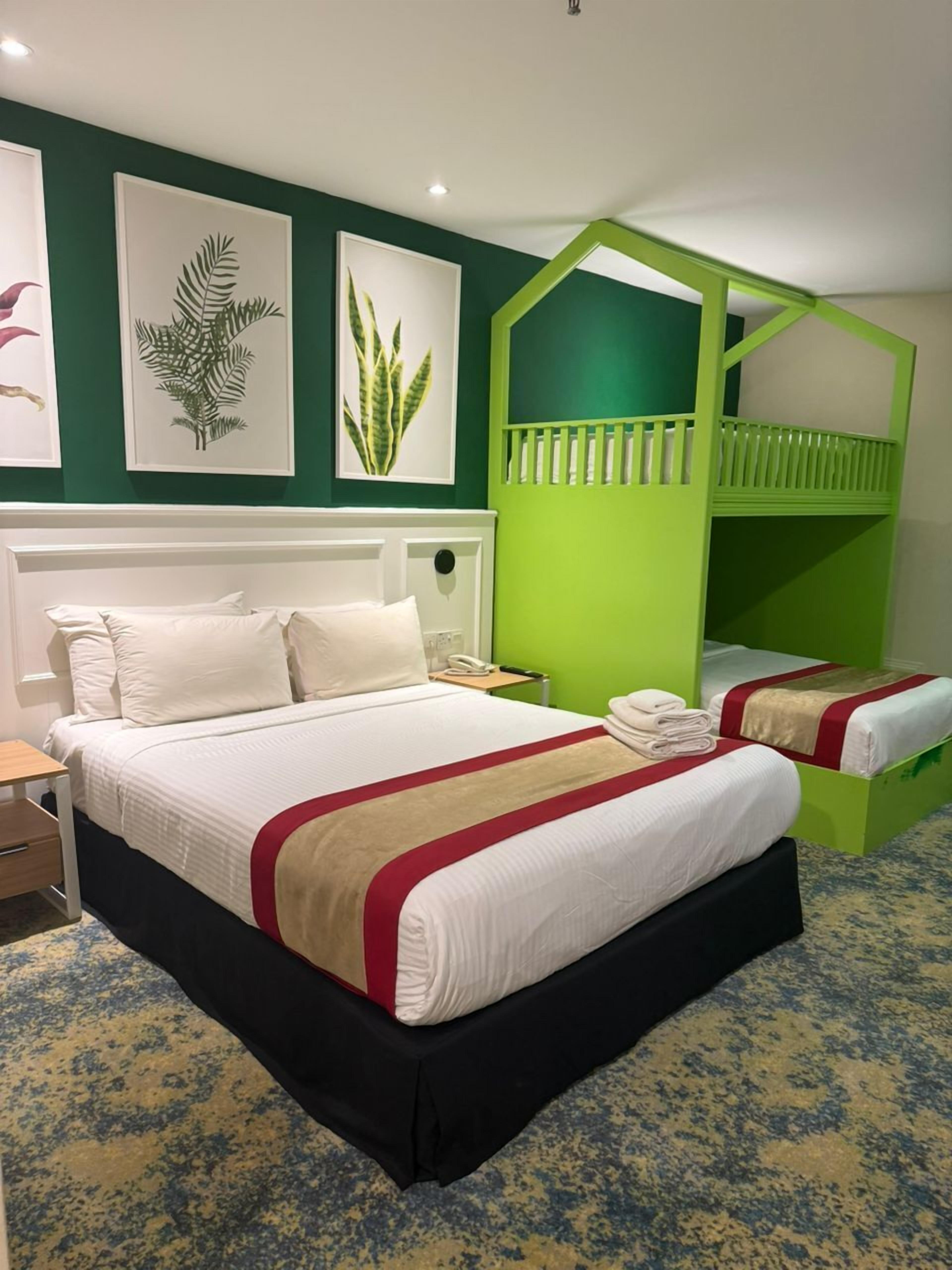 A hotel room with a large bed, a green bunk bed, and three framed plant prints on the wall.