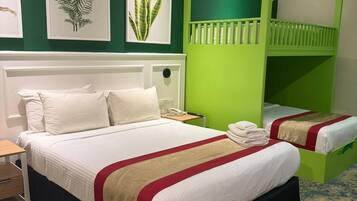 A hotel room with a large bed, a green bunk bed, and three framed plant prints on the wall.