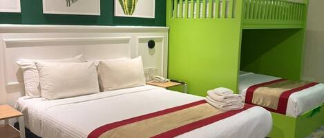 A hotel room with a large bed, a green bunk bed, and three framed plant prints on the wall.