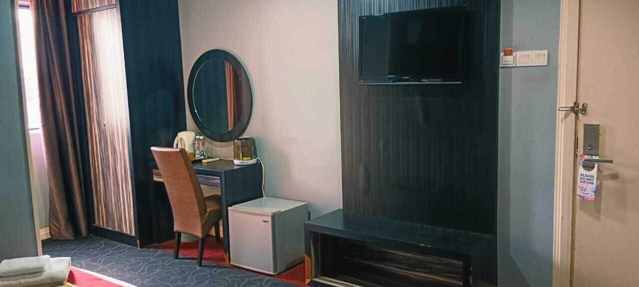 A hotel room with a desk, chair, television, and a small refrigerator.