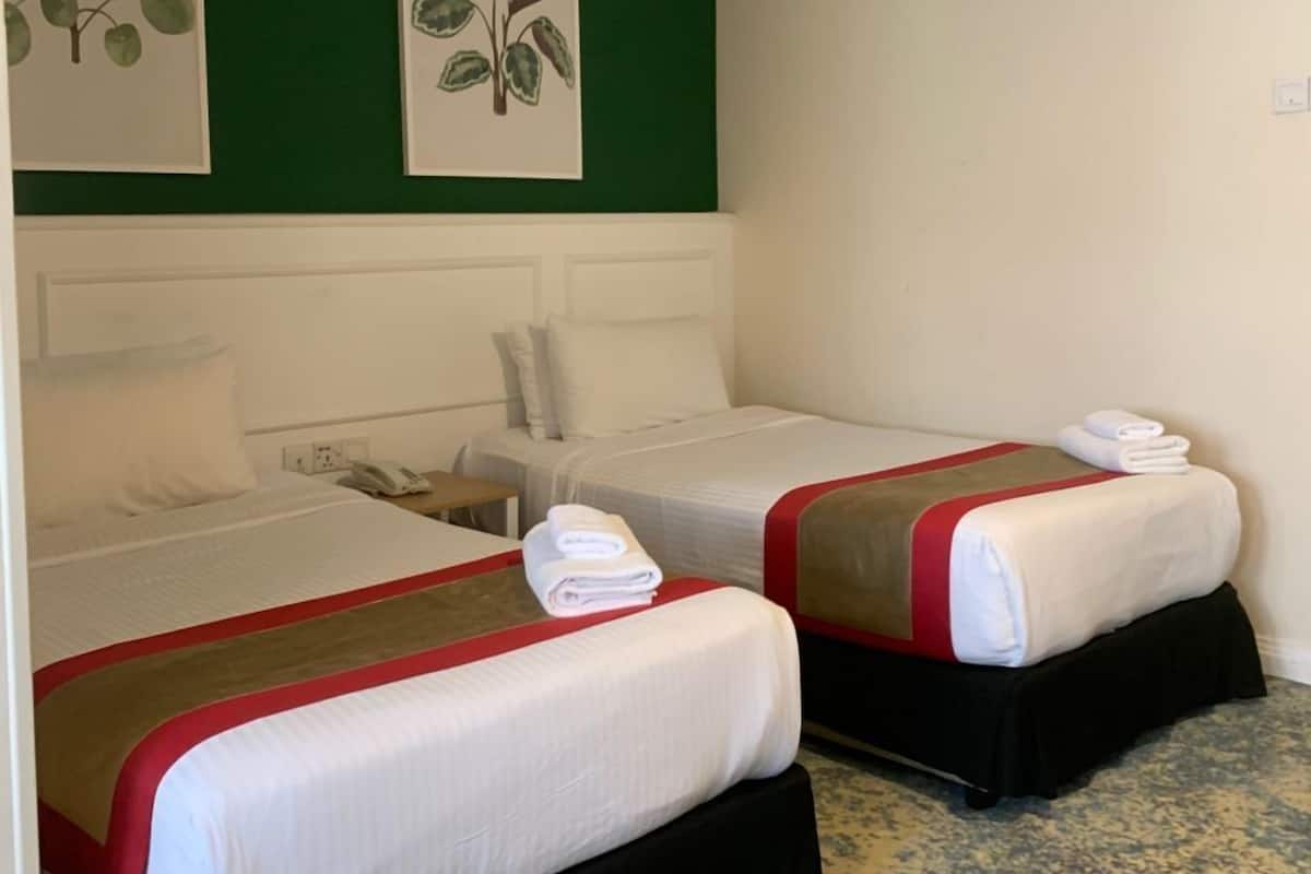 A hotel room with two beds, green walls, and artwork of leaves.
